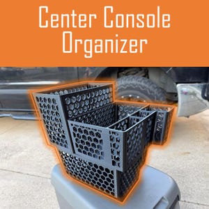 May include: Black centre console organiser with a honeycomb pattern. The organiser has multiple compartments and the text "Center Console Organizer" in white letters on an orange background.