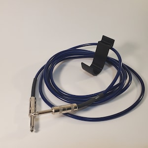 Könnte beinhalten: Ein blaues Gitarrenkabel mit einem schwarzen Kabelhaken. Das Kabel hat an einem Ende einen 6,35-mm-Stecker und am anderen Ende eine 6,35-mm-Buchse.