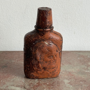 Pocket flask liquor bottle covered with leather. 16.5x8.5x4 cm (6.5 inch height) Glass bottle covered with leather. Relief embossed decoration head