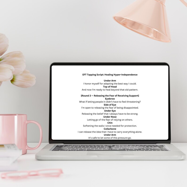 Pu&ograve; includere: Un laptop mostra uno script di tapping EFT per la guarigione dall'iper-indipendenza. Lo schermo mostra testo con frasi come "Sotto il braccio", "Sommit&agrave; della testa" e "Lato dell'occhio". Una tazza rosa e una penna sono sulla scrivania.