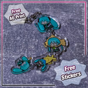 May include: A clear acrylic keychain featuring three anime-style figures with turquoise hair. The figures are connected by a silver chain. The image also includes text that says "Free A6 Print" and "Free Stickers".