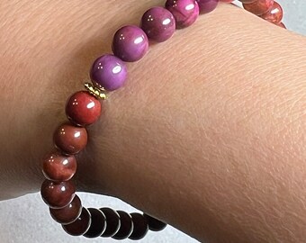 May include: A bracelet made of red, purple, and brown beads. The beads are round and have a smooth finish. The bracelet is worn on a person's wrist.