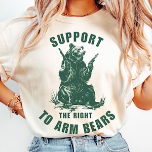 May include: A white t-shirt with a green graphic of a bear holding two guns. The text "SUPPORT THE RIGHT TO ARM BEARS" is printed on the shirt.