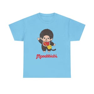 A light blue short-sleeved t-shirt isolated on a white background, displaying a Monchhichi graphic and red text.