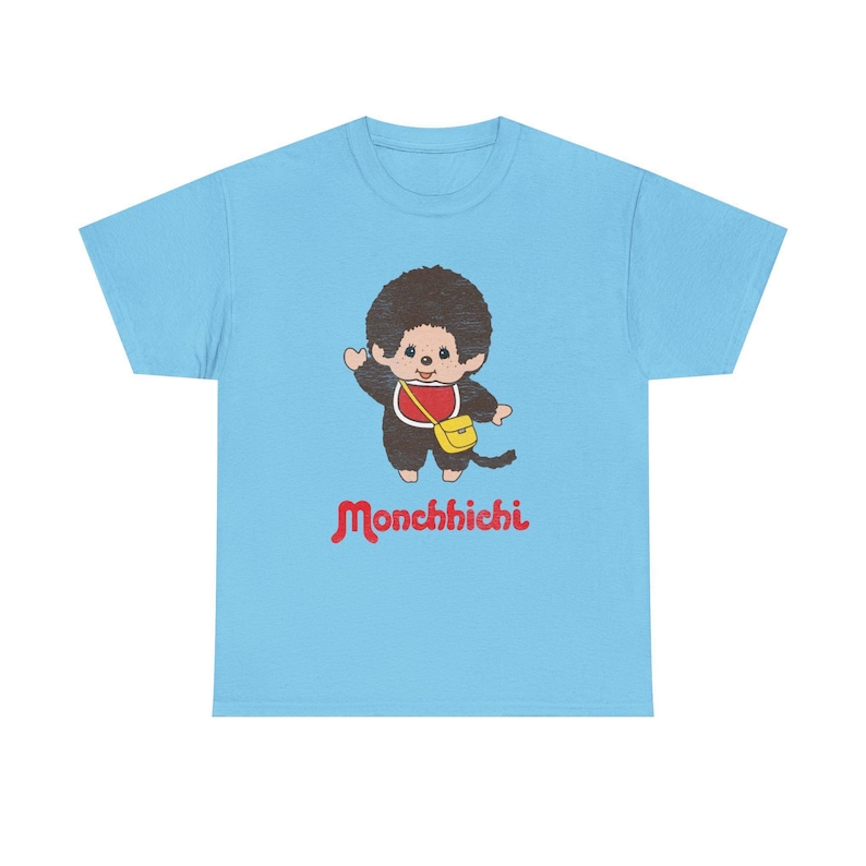 A light blue short-sleeved t-shirt isolated on a white background, displaying a Monchhichi graphic and red text.