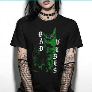 Front view of a person in a black graphic t-shirt with a green cat and the text Bad Vibes.