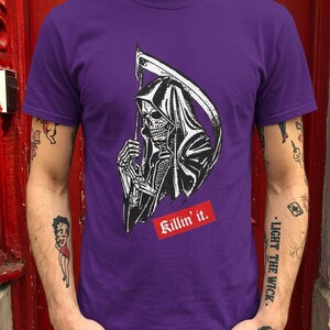 A person wearing a purple t-shirt featuring a grim reaper illustration and red text.