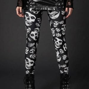 A person wearing black leggings with a white skull and skeleton hand print, a laced black leather skirt, and black platform boots.