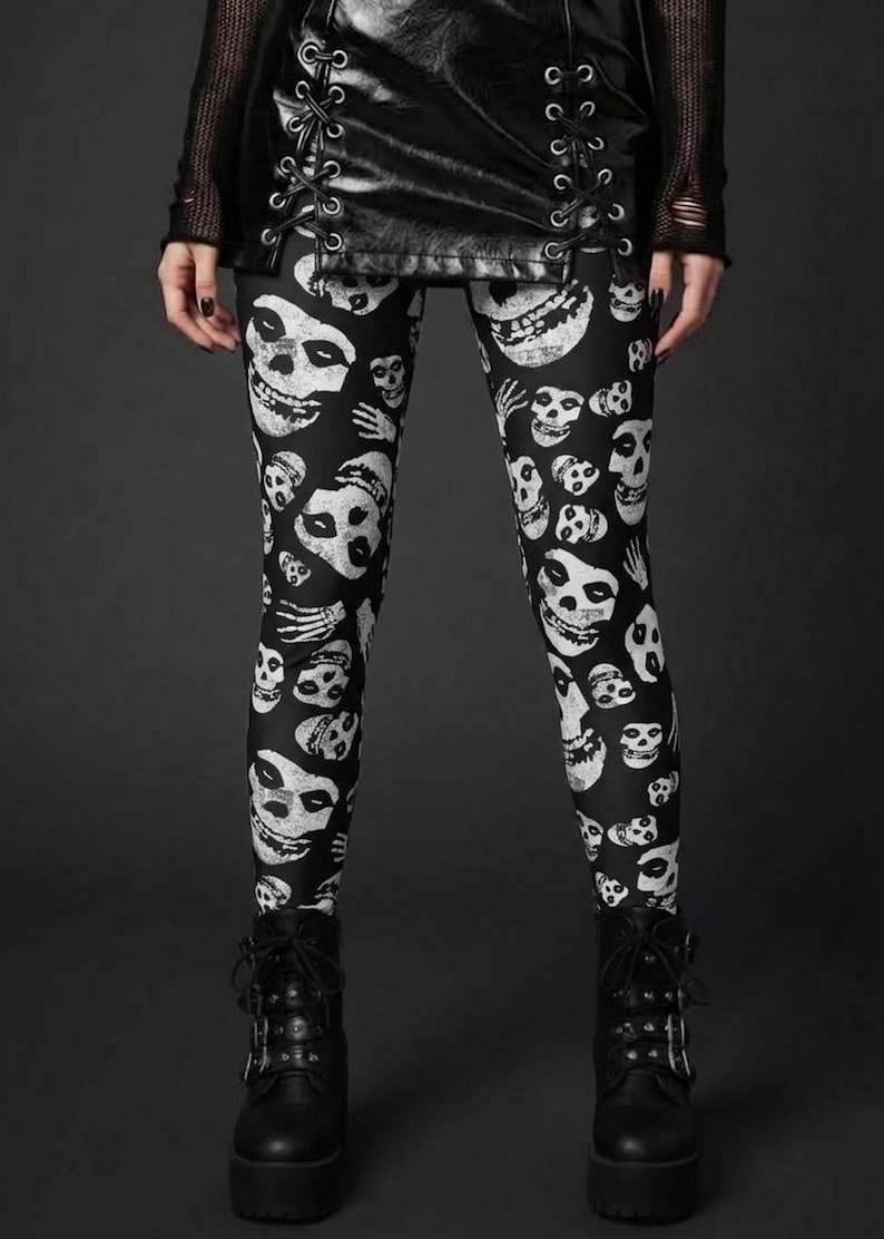 A person wearing black leggings with a white skull and skeleton hand print, a laced black leather skirt, and black platform boots.
