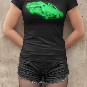 May include: A black short-sleeved t-shirt featuring a glowing neon green graphic of a vintage car positioned at an angle. The car illustration is centered on the chest area, showcasing a detailed side profile of the vehicle with a bright, luminous effect.
