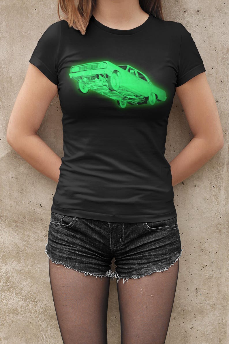 May include: A black short-sleeved t-shirt featuring a glowing neon green graphic of a vintage car positioned at an angle. The car illustration is centered on the chest area, showcasing a detailed side profile of the vehicle with a bright, luminous effect.