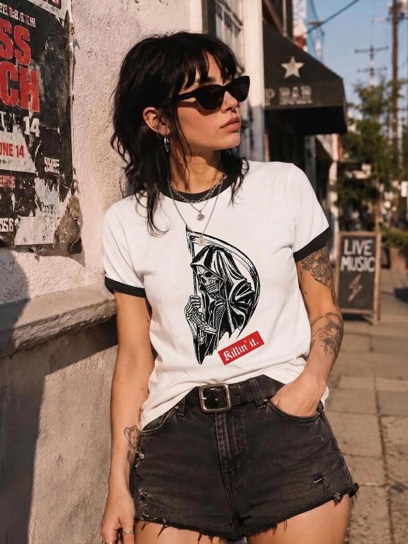 A person wearing sunglasses and a white ringer tee with black trim, printed with a black grim reaper graphic and a red text box that reads Killin it.