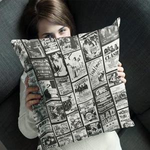 May include: Black and white pillow featuring a collage of vintage concert posters. The pillow displays various band names and concert details, creating a retro aesthetic. The pillow is rectangular and appears to be made of a soft fabric.