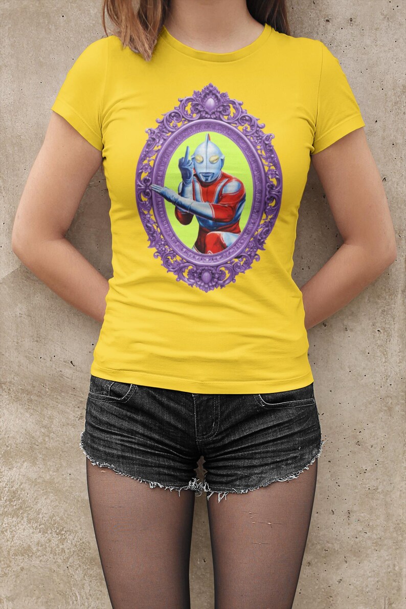 May include: Yellow t-shirt with a framed graphic of a superhero in red, blue, and silver. The oval frame is purple. The shirt is worn with black denim shorts.