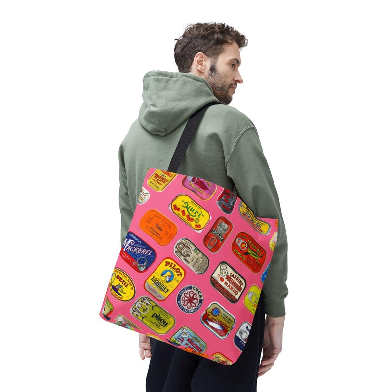 A person in a green hoodie and black shorts carries a pink tote bag with sardine can labels over their left shoulder, viewed from behind.