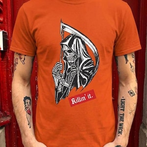 A person wearing a burnt orange t-shirt with a graphic of the grim reaper and the text Killin it in red.