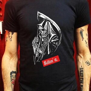 A person wearing a black t-shirt printed with a graphic of a grim reaper in a hood holding a scythe.