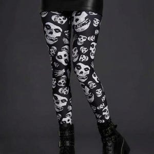 A person wearing black leggings featuring a white skull pattern, a black miniskirt, and black platform combat boots.