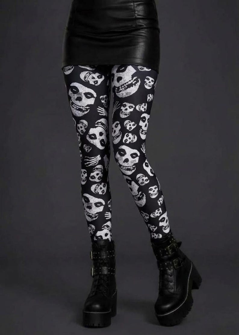 A person wearing black leggings featuring a white skull pattern, a black miniskirt, and black platform combat boots.