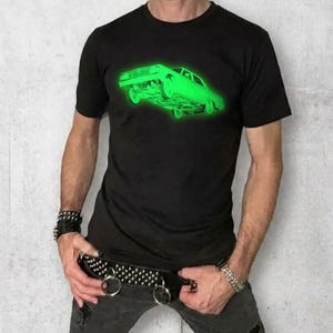May include: A black short-sleeved t-shirt featuring a bright neon green graphic of a classic car on the chest. The shirt is paired with dark gray distressed jeans and a wide black belt adorned with silver metal studs and two large metal rings.