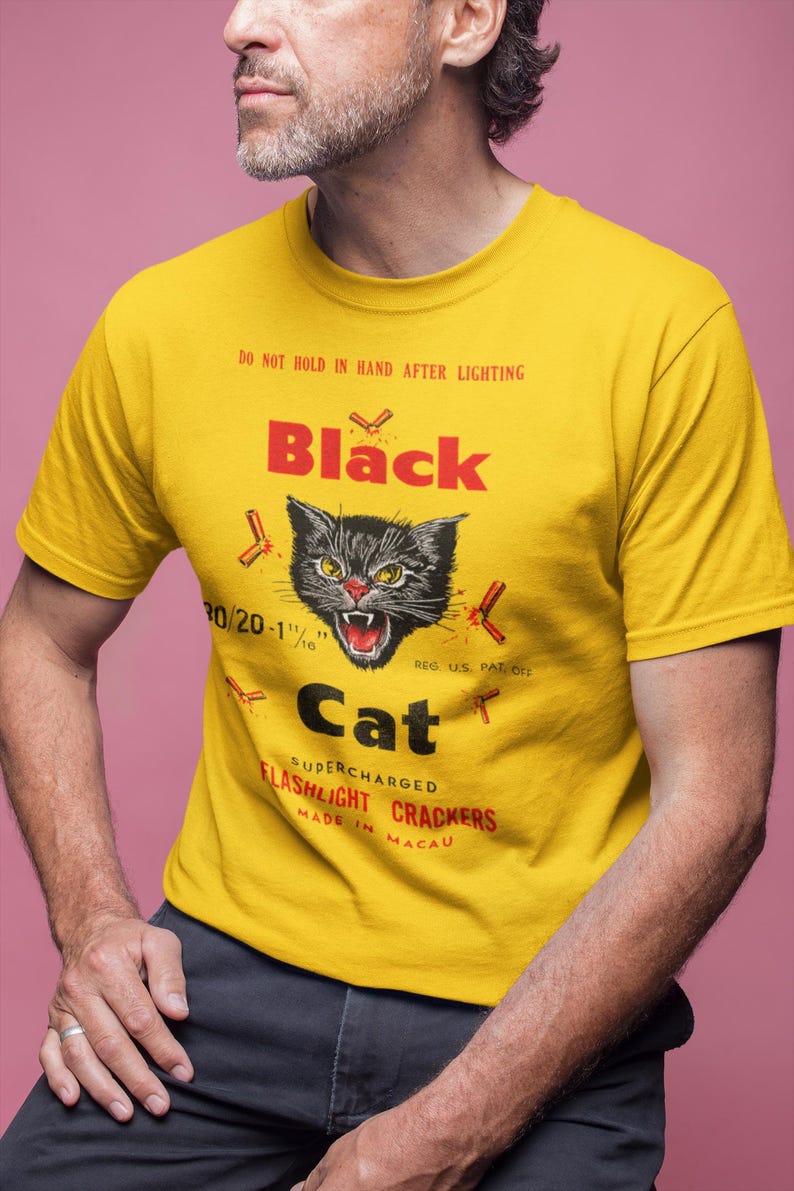 May include: Yellow t-shirt featuring a black cat graphic with red accents and the text "Black Cat Flashlight Crackers". The shirt also has the text "Do not hold in hand after lighting".