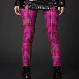 A person wearing pink plaid leggings, a laced black leather mini skirt, and black platform boots.