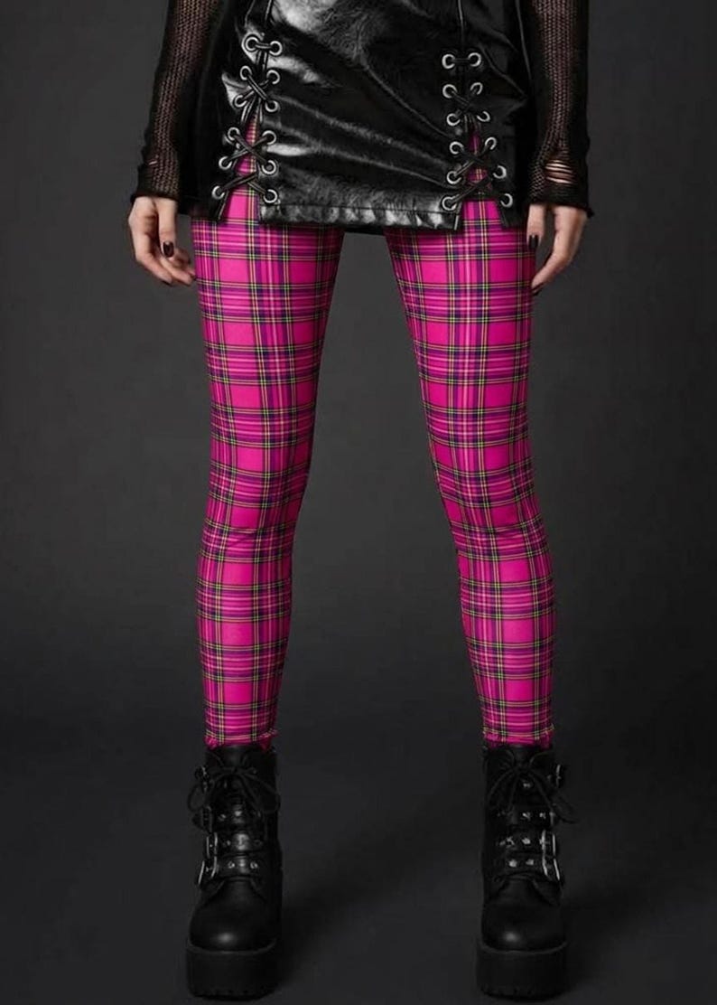 A person wearing pink plaid leggings, a laced black leather mini skirt, and black platform boots.