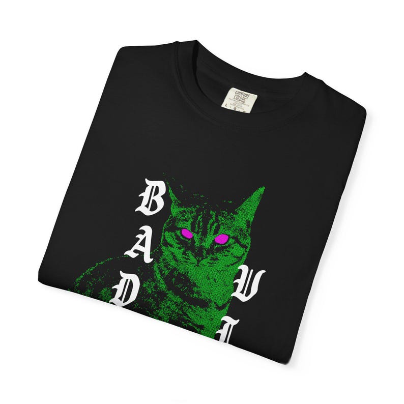 A neatly folded black t-shirt showing a close-up of the green cat graphic and white text on the chest.