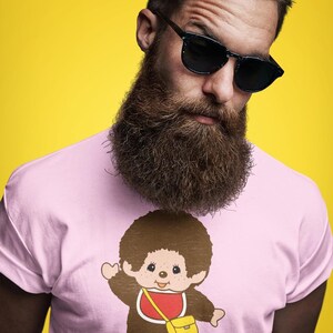 A man with a large beard and sunglasses wears a light pink t-shirt featuring a Monchhichi graphic against a yellow background.