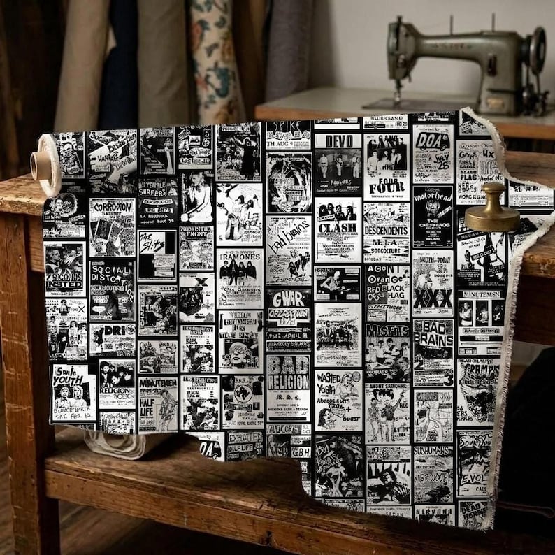 A bolt of punk flyer collage fabric rests on a wooden table next to a sewing machine.