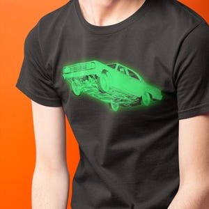 May include: A black short-sleeved t-shirt featuring a glowing neon green graphic of a vintage car positioned at an angle. The car illustration shows the front and side profile with a bright, luminous effect against the dark fabric of the shirt.