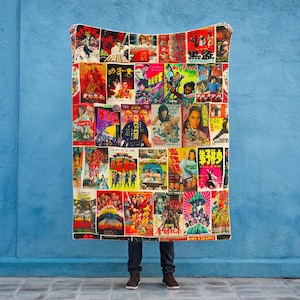 A person holds up a blanket patterned with a collage of vintage Kung Fu movie posters against a blue wall.