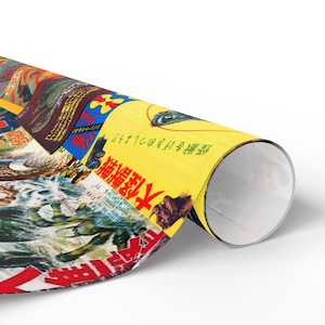 A roll of Godzilla-themed wrapping paper, partially unrolled, showing a collage of vintage movie posters with Japanese text.