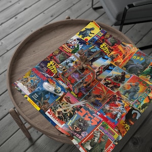 A flat sheet of Godzilla-themed wrapping paper, with a small gift wrapped in the same paper and tied with a brown ribbon, on a round wooden table.