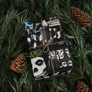 A gift wrapped in black and white Misfits-themed paper with twine, resting on green pine branches with pinecones.