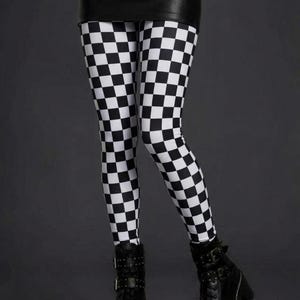A person wearing black and white checkerboard leggings, a black faux leather skirt, and black platform boots.