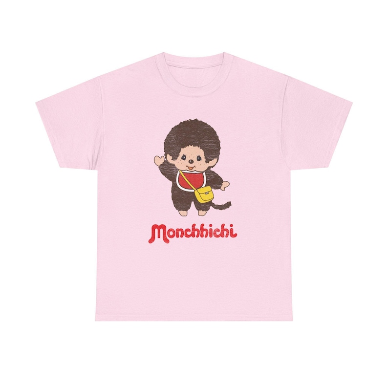 A light pink short-sleeved t-shirt displayed on a white background, featuring a cartoon monkey graphic and red Monchhichi text.