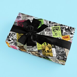 May include: A gift box wrapped in black and white patterned paper with a black ribbon. The paper features a collage of concert posters with band names like "The Damned", "Black Flag", "Dickies", and "GBH".