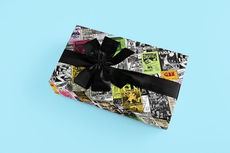 May include: A gift box wrapped in black and white patterned paper with a black ribbon. The paper features a collage of concert posters with band names like "The Damned", "Black Flag", "Dickies", and "GBH".