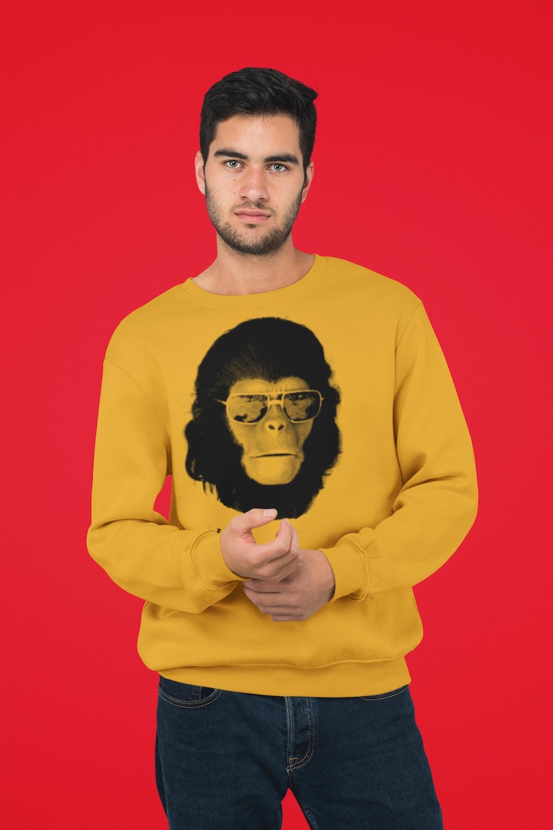 K&ouml;nnte beinhalten: Senfgelbes Sweatshirt mit einem schwarz-wei&szlig;en Grafik eines Affen mit Sonnenbrille. Das Gesicht des Affen ist mittig auf der Vorderseite des lang&auml;rmeligen Rundhalsausschnitts. Der Hintergrund ist einfarbig rot.