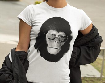 May include: A white short-sleeved t-shirt featuring a large, centered black and white graphic print of a chimpanzee wearing silver-rimmed sunglasses. The graphic is detailed with high-contrast shading, showcasing the primate's facial features.