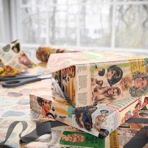 May include: Two rectangular boxes wrapped in vintage-style paper featuring images of women's hairstyles and the text "100% Human Hair." The boxes are on a table with matching wrapping paper, scissors, and a black ribbon.
