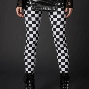 A person wearing black and white checkerboard leggings, a laced black leather mini skirt, and black platform boots.