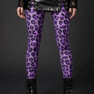 A person wearing vibrant purple leopard print leggings paired with a black lace-up skirt and platform boots.
