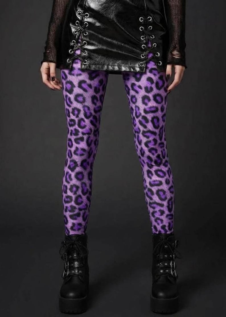 A person wearing vibrant purple leopard print leggings paired with a black lace-up skirt and platform boots.
