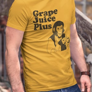 May include: Mustard yellow t-shirt with the text "Grape Juice Plus" and a black and white illustration of a chimpanzee holding a glass. The shirt is a short-sleeved crew neck.