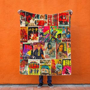 A person holds up a blanket patterned with a collage of vintage Kung Fu movie posters against an orange wall.