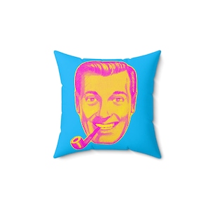 A square blue throw pillow with a magenta and yellow pop-art style face of a man smoking a pipe is centered on a white background.