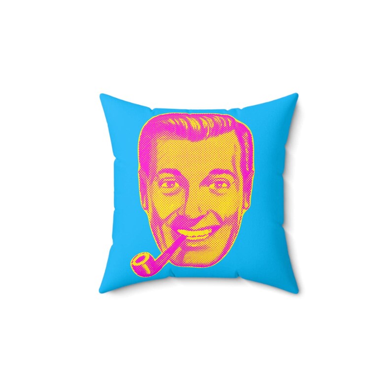 A square blue throw pillow with a magenta and yellow pop-art style face of a man smoking a pipe is centered on a white background.