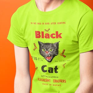 May include: A lime green t-shirt with a graphic of a black cat and the text "Black Cat". The design includes the text "Do Not Hold In Hand After Lighting" and "Flashlight Crackers". The shirt is made in Macau.